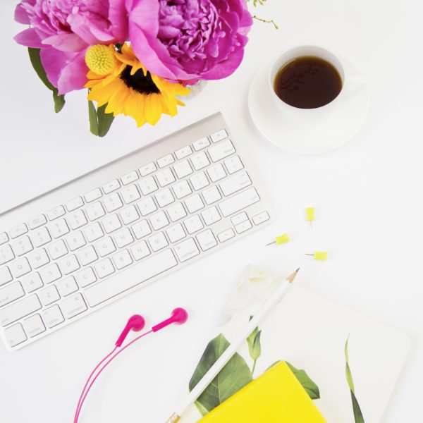 white keyboard with desk accessories, cup of coffee, and pink flowers