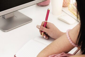 woman sitting at a desk in front of a computer writing in a notebook